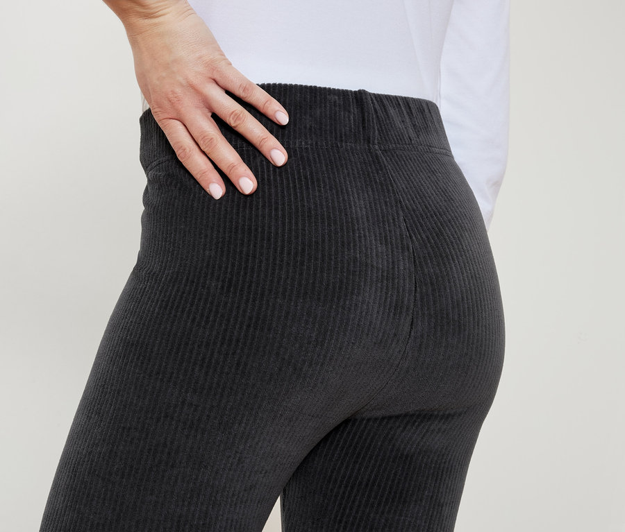 Frau in grauer Cordhose legt ihre Hand auf ihre Hüfte.