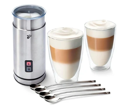 Ein Edelstahl-Milchaufschäumer neben zwei Gläsern mit Kaffee und Milchschaum und vier Löffeln. Zu sehen ist das Milchschäum-Set "Cremige Versuchung".