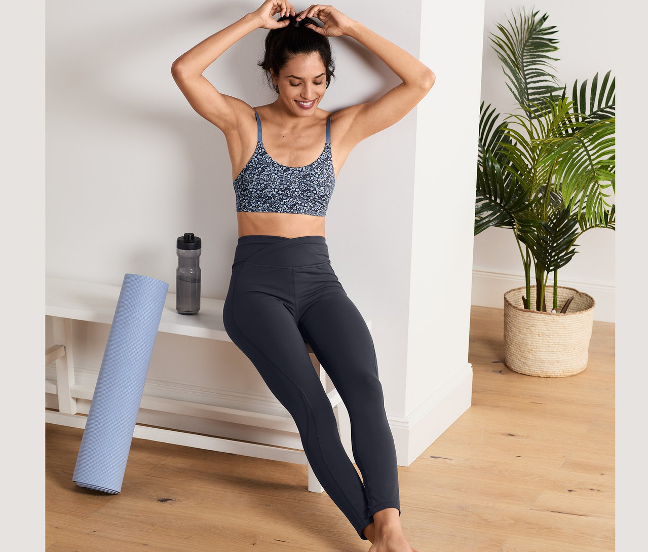 Frau macht ihre Haare. Sie trägt einen Sport-BH und eine Sporttight.