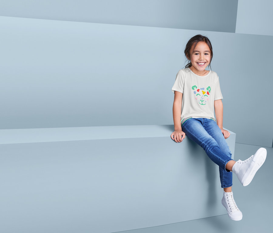 Ein lächelndes Mädchen sitzt und trägt ein T-Shirt in Schlupfform, Jeans und Schuhe.