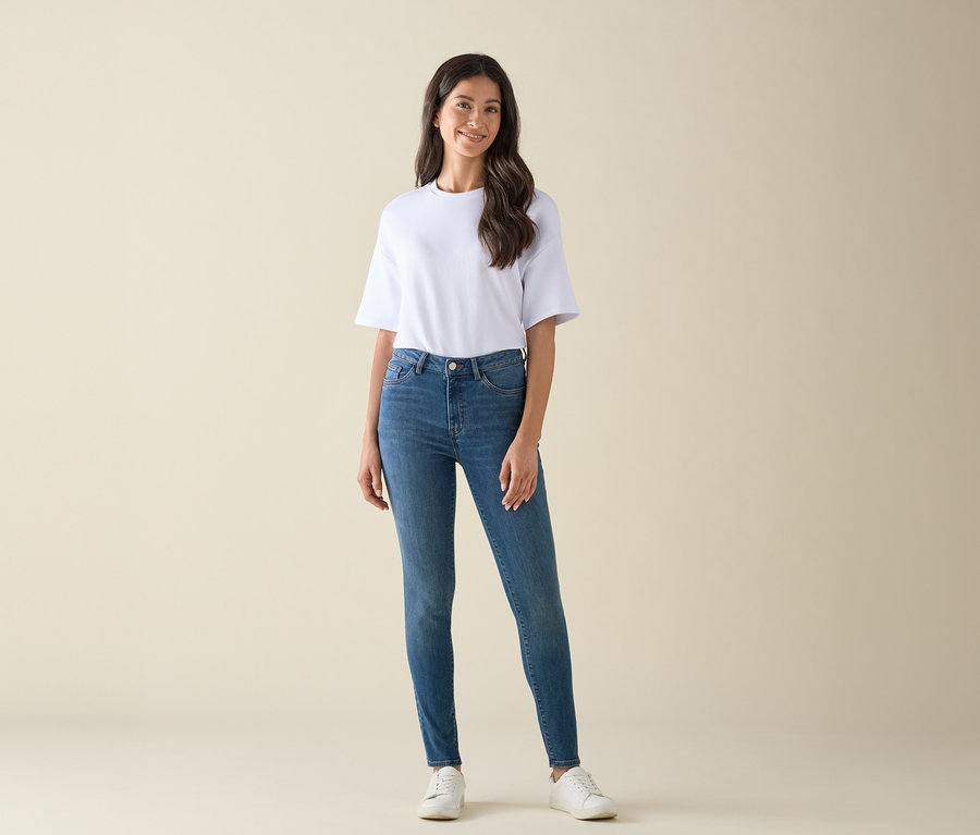 Frau posiert in einem weißen T-Shirt, blauen Jeans und weißen Turnschuhen.