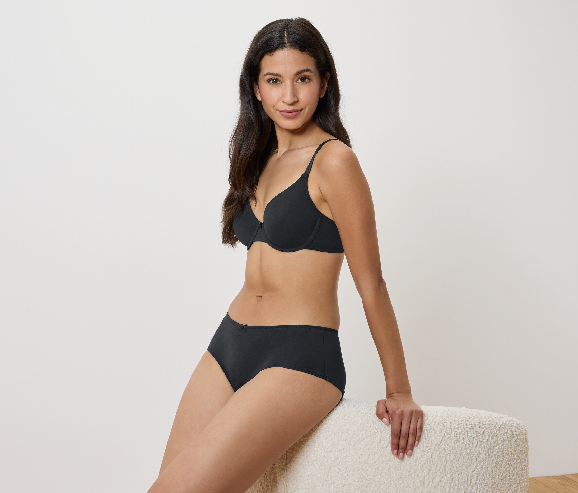 Frau sitzt auf einem Hocker in schwarzem BH und Unterhose.