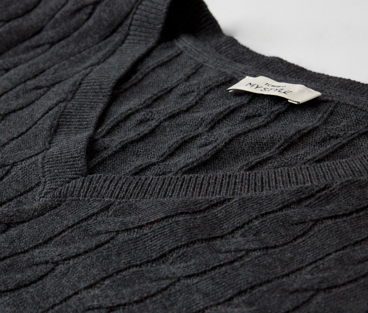 Detailaufnahme eines grauen Zopfmusterpullovers mit V-Ausschnitt.