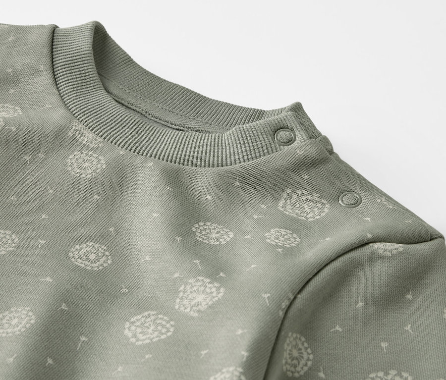 Detailansicht eines grünen Sweat-Kombis mit Löwenzahn-Print.