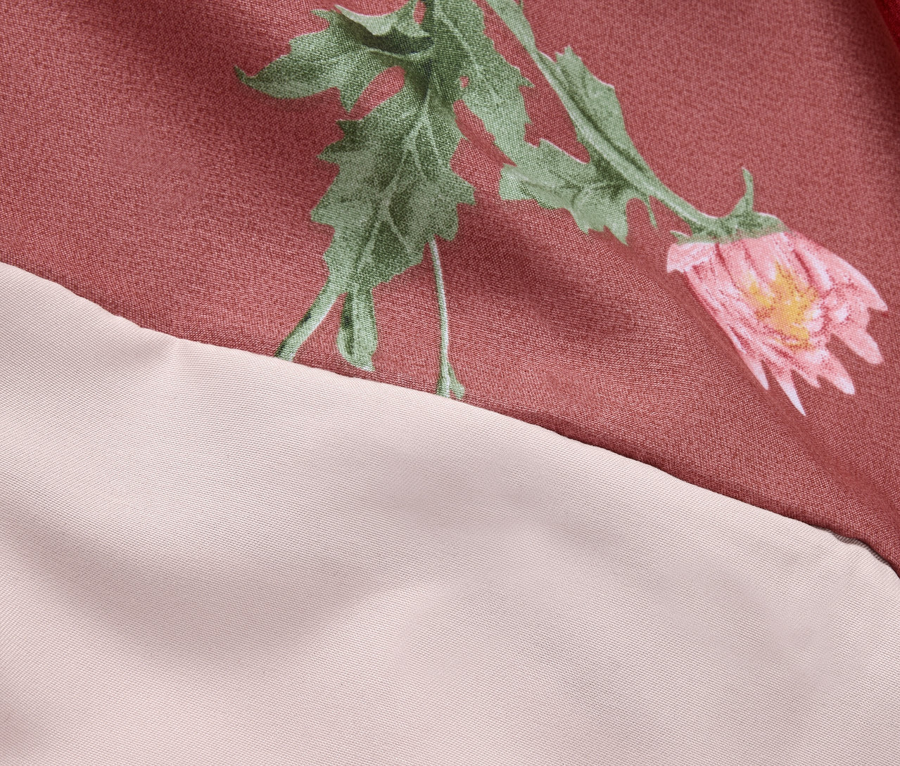 Detailaufnahme eines rosafarbenen Stoffes mit Blumenmuster und cremefarbenem Rand.