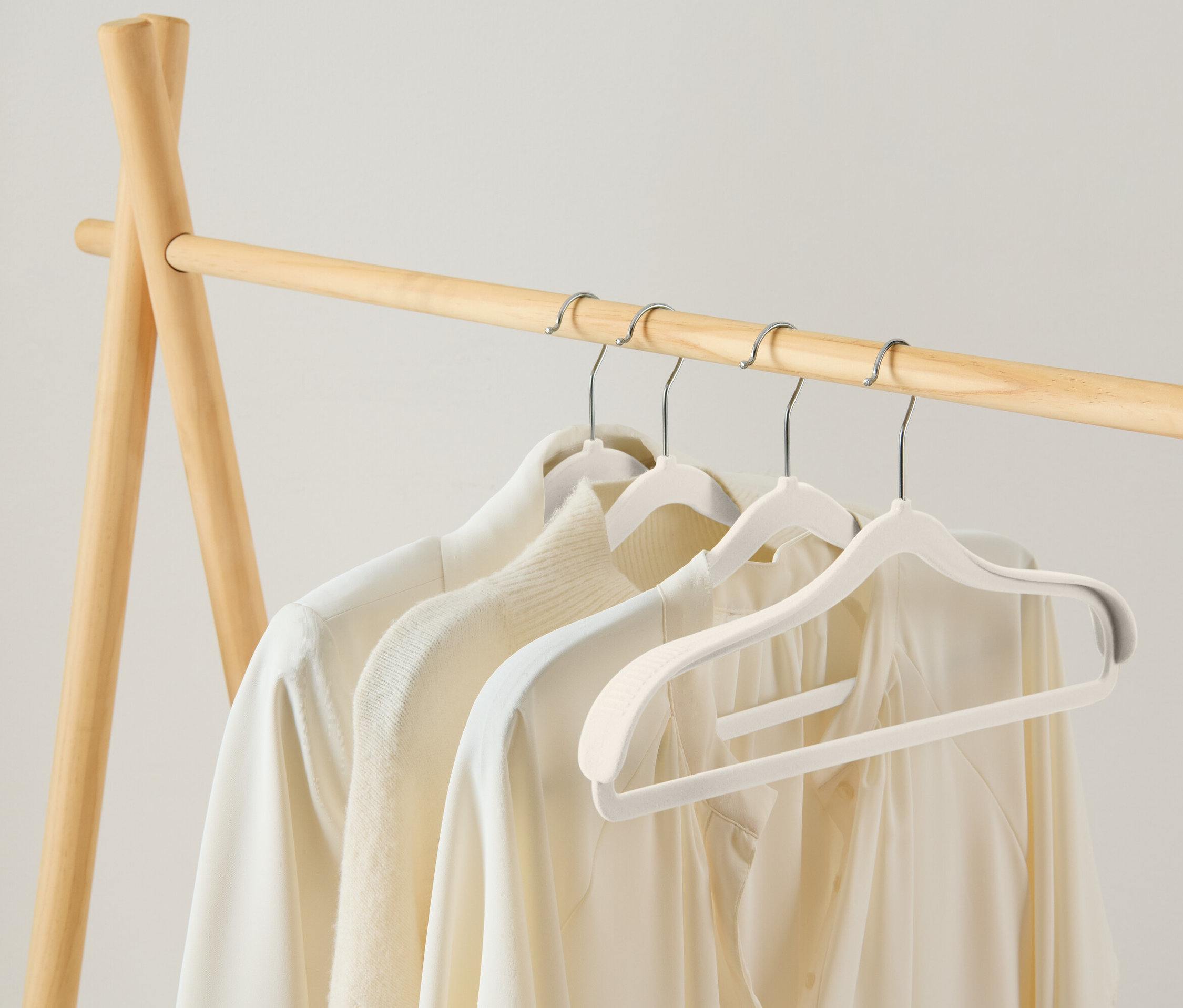 Drei weiße Blusen hängen auf weißen Kleiderbügeln an einer hölzernen Kleiderstange.