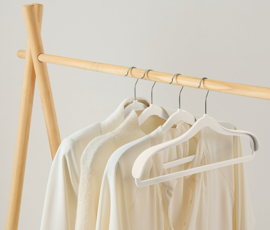 Drei weiße Blusen hängen auf weißen Kleiderbügeln an einer hölzernen Kleiderstange.