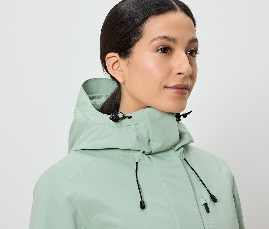 Frau trägt eine hellgrüne Jacke mit Kapuze.