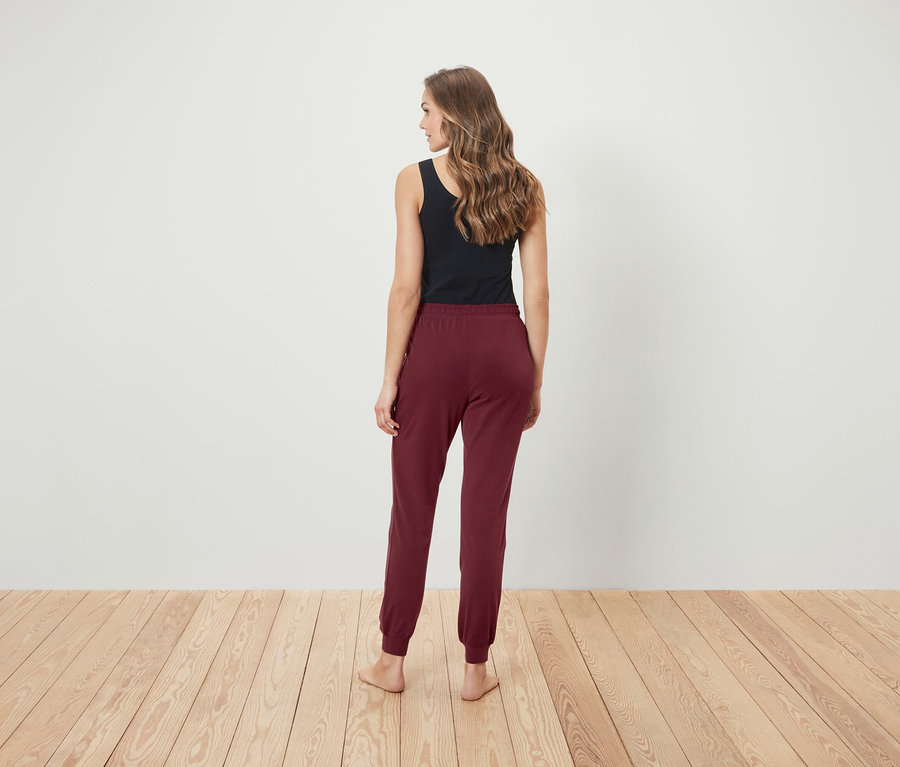 Frau steht mit dem Rücken zum Betrachter und trägt ein schwarzes Tanktop und weinrote Trainingshose.
