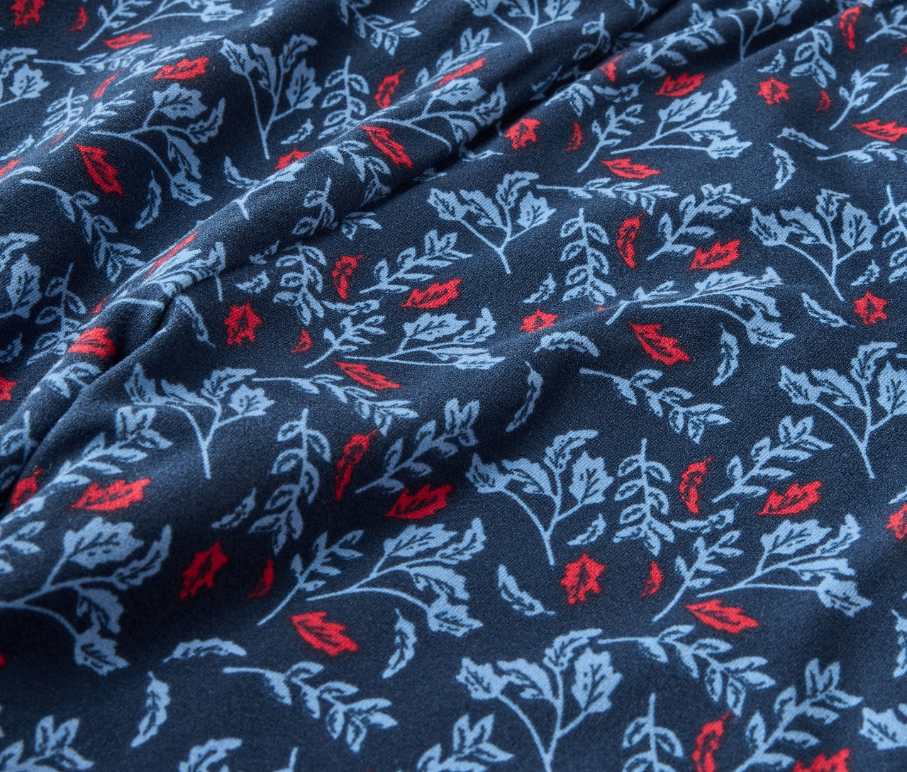 Nahaufnahme eines dunkelblauen Stoffes mit einem Aufdruck aus roten und hellblauen Blättern.