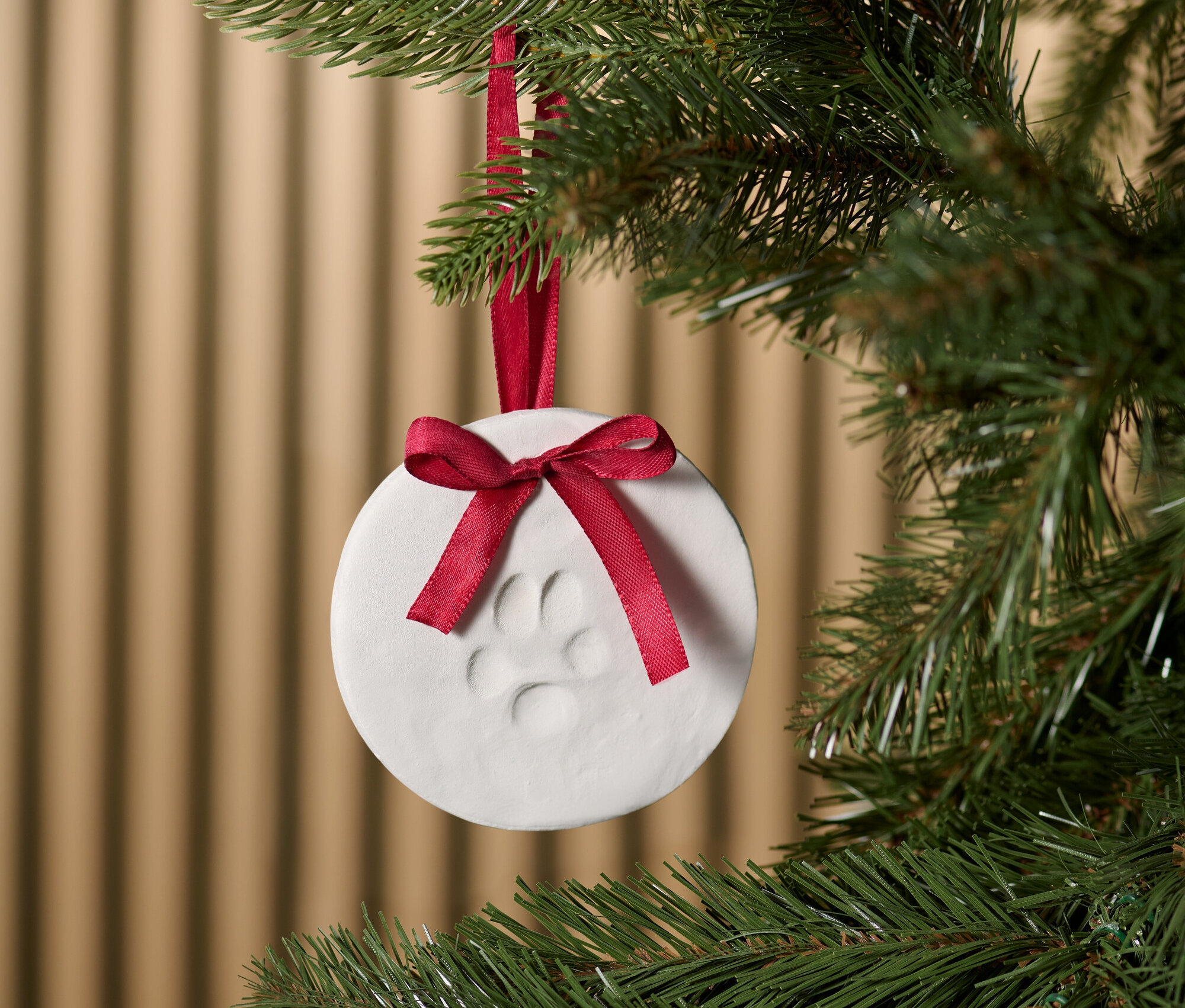 An einem Weihnachtsbaum hängt ein weißer Anhänger mit einem Pfotenabdruck und einem roten Band.