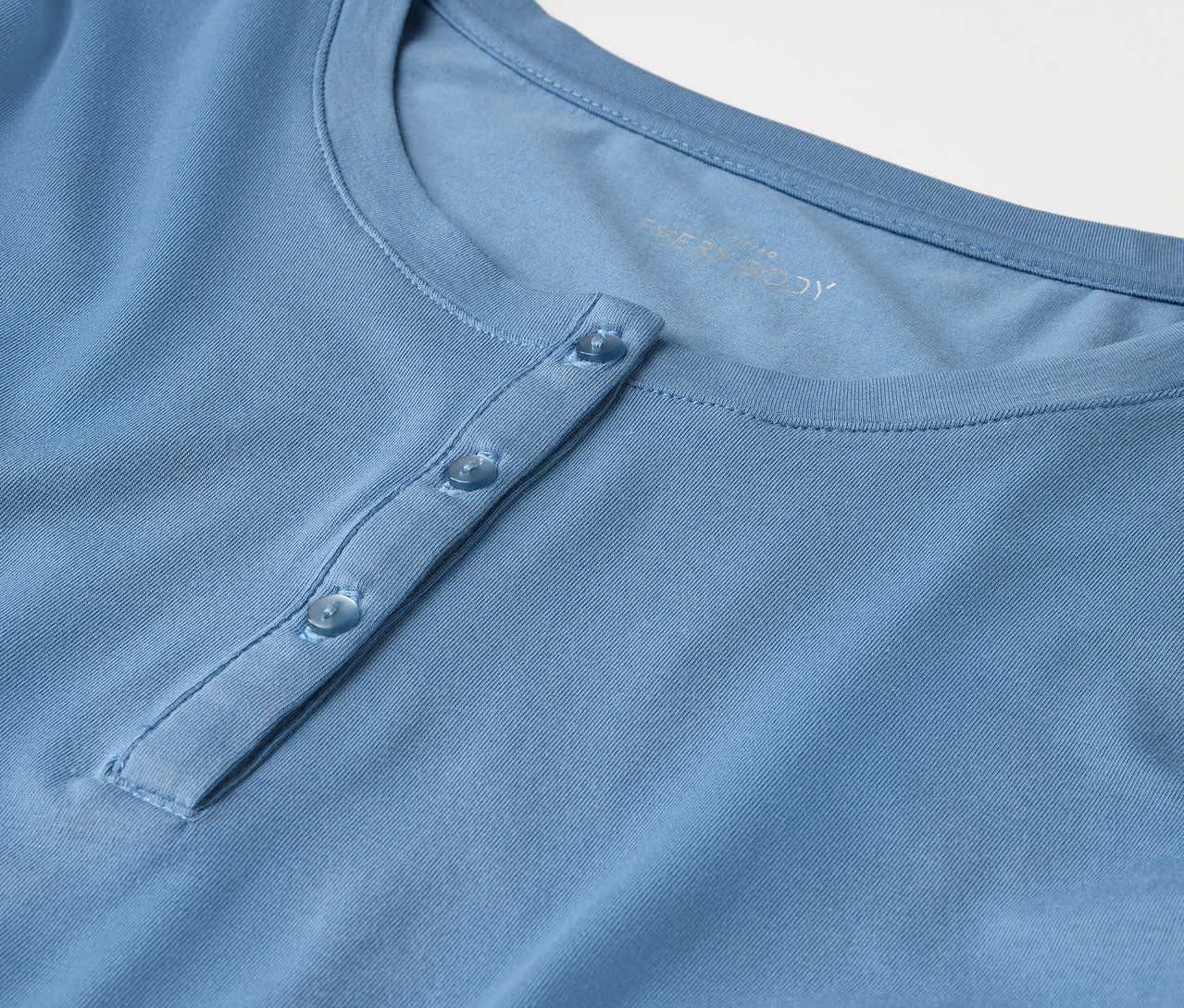 Detailaufnahme eines hellblauen T-Shirts mit Knöpfen.