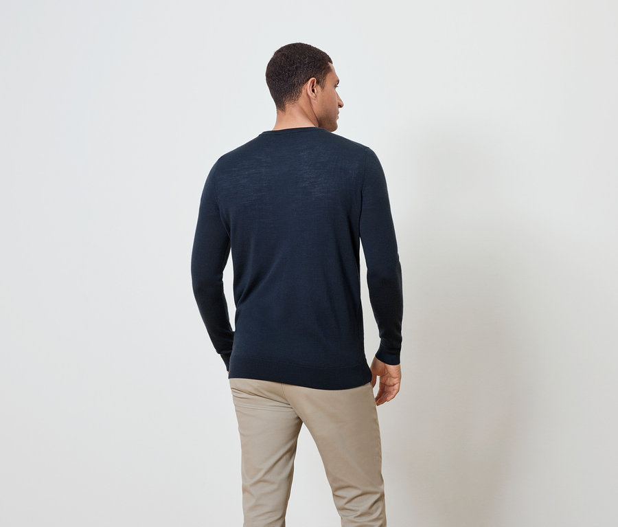 Ein Mann von hinten, gekleidet in einem dunkelblauen Pullover und beigen Hosen.