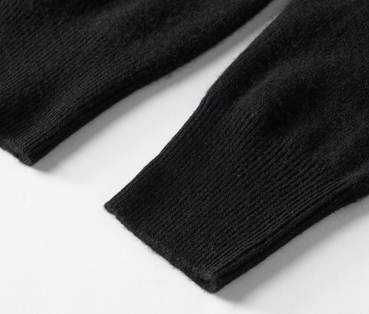 Detailaufnahme eines schwarzen Strickärmels eines Pullovers.