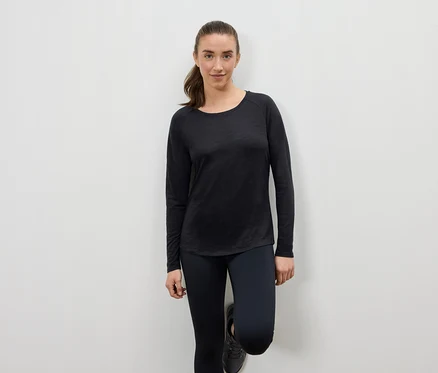 Frau in schwarzer Sportbekleidung, die sich an eine Wand lehnt.