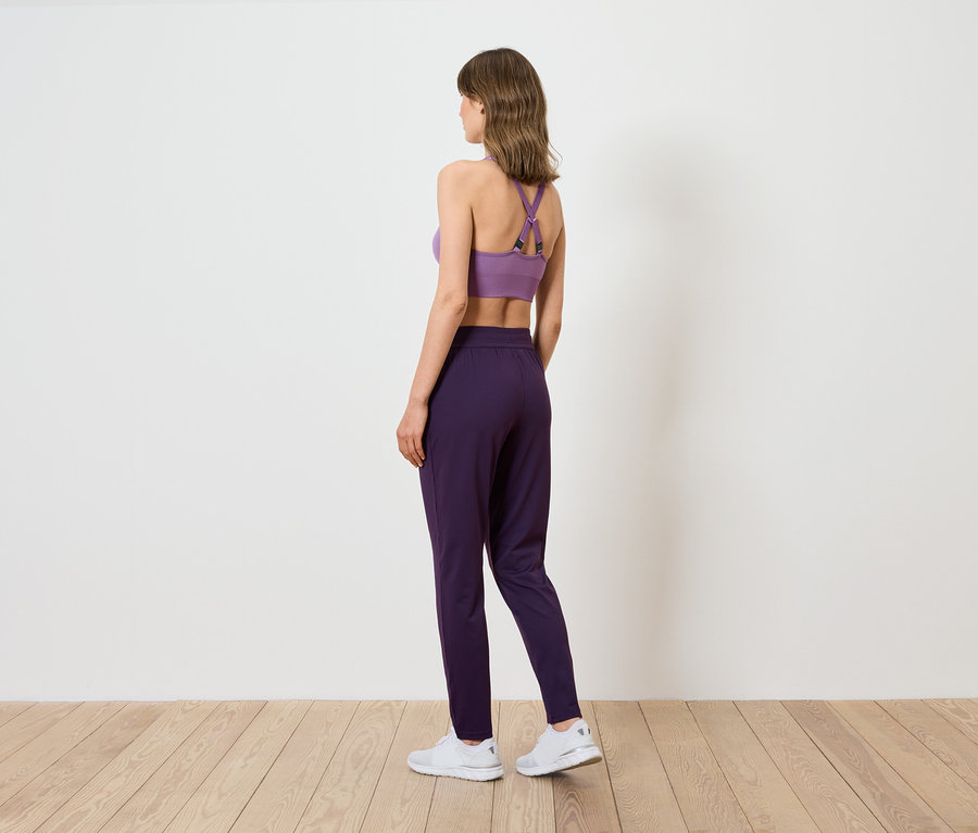 Eine Frau von hinten, die einen lila Sport-BH und dunkelviolette Hosen trägt.