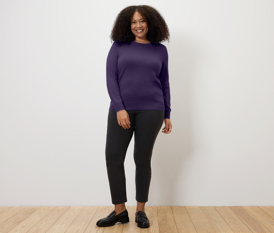 Frau trägt Feinstrickpullover mit Cashmere, pflaume, dazu eine schwarze Hose und schwarze Slipper.