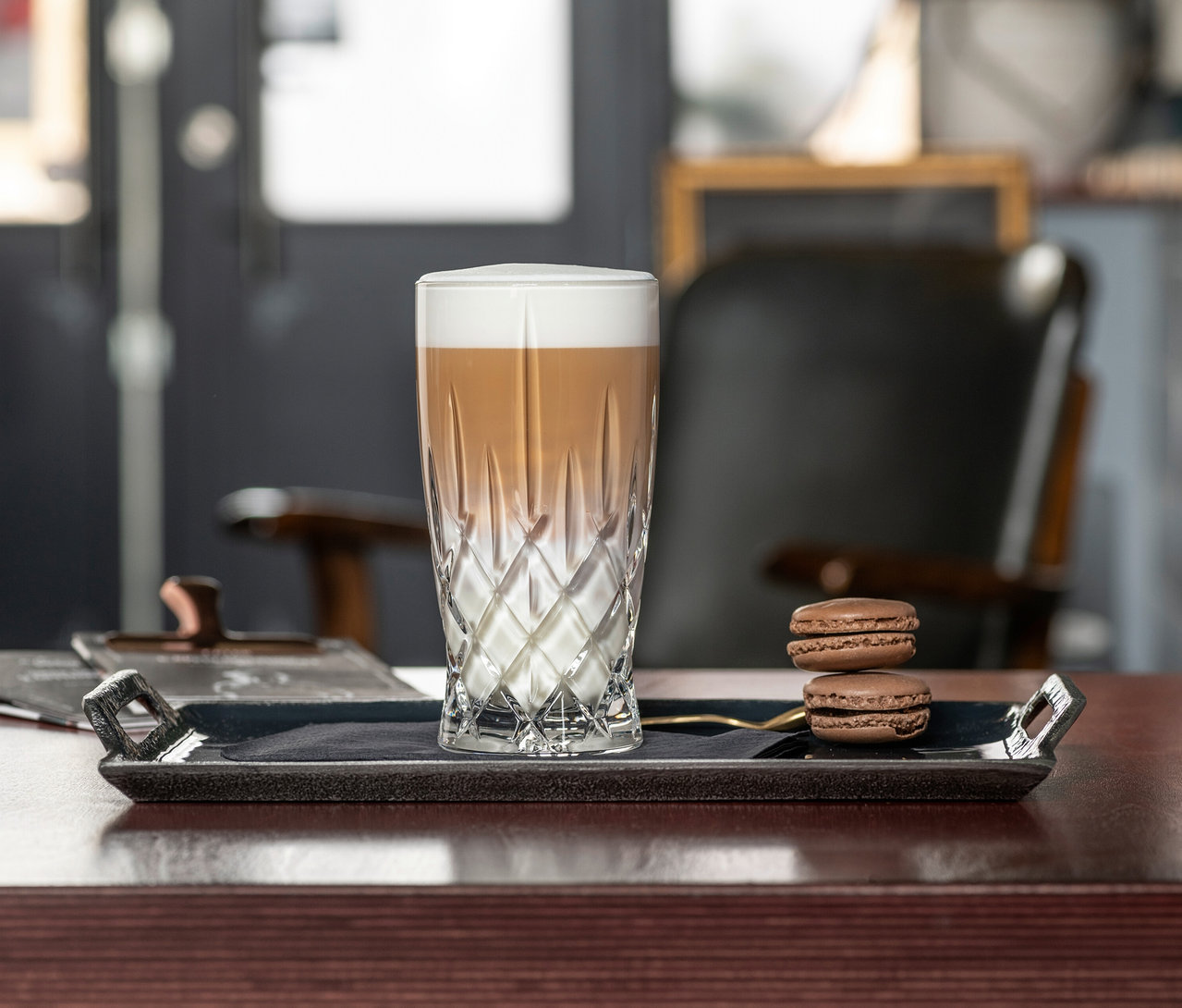 Ein Nachtmann Latte-Macchiato-Glas »Noblesse« mit Latte Macchiato und zwei Macarons auf einem Serviertablett.