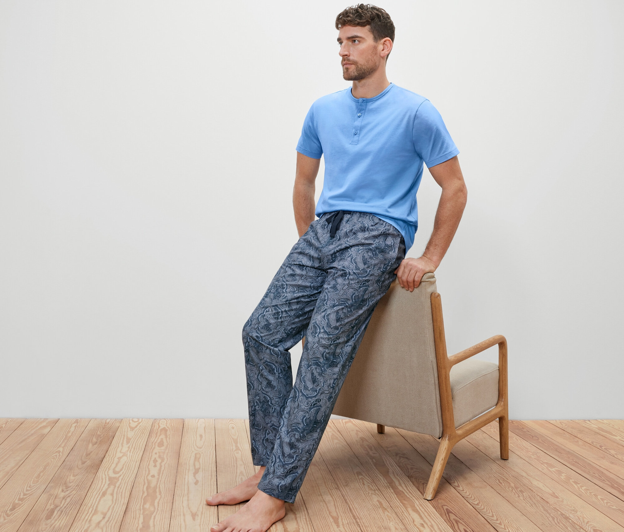 Mann sitzt auf einem Sessel und trägt ein Pyjama-Set mit gewebter Hose.