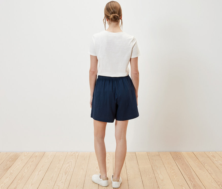 Frau von hinten in Musselin-Shorts und weißem T-Shirt.