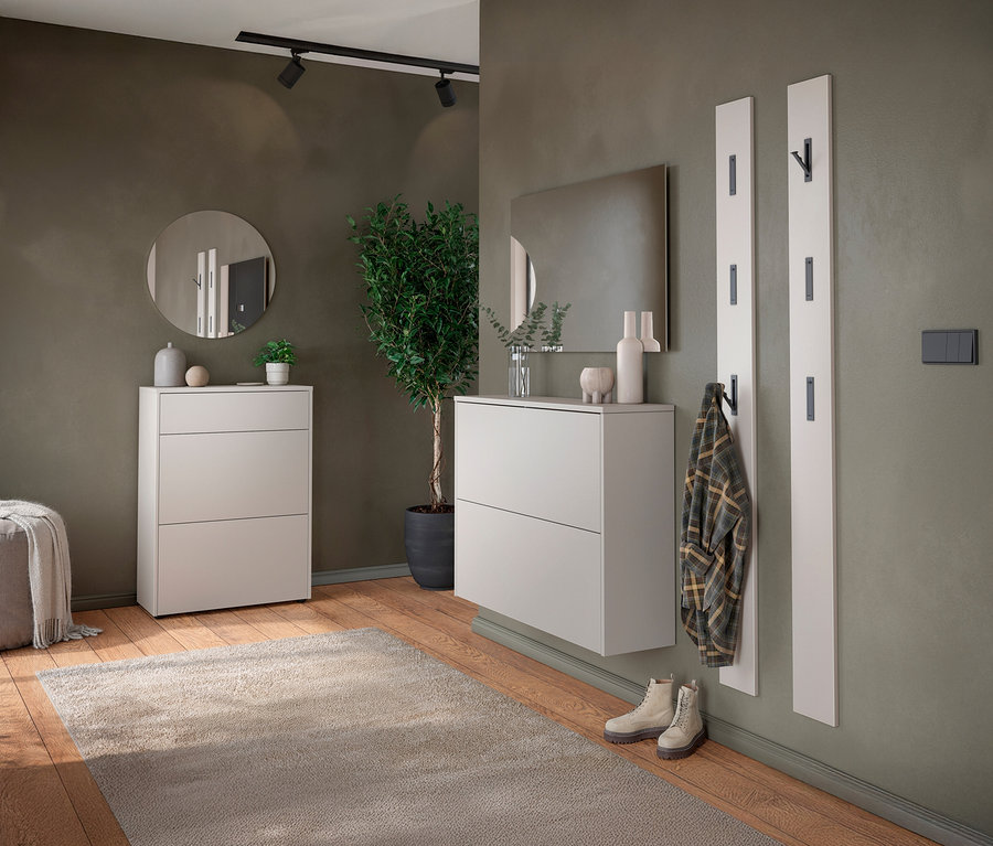 Flur mit zwei weißen Schuhschränken, einem runden Spiegel, einer Zimmerpflanze und einer Garderobe mit Jacke.