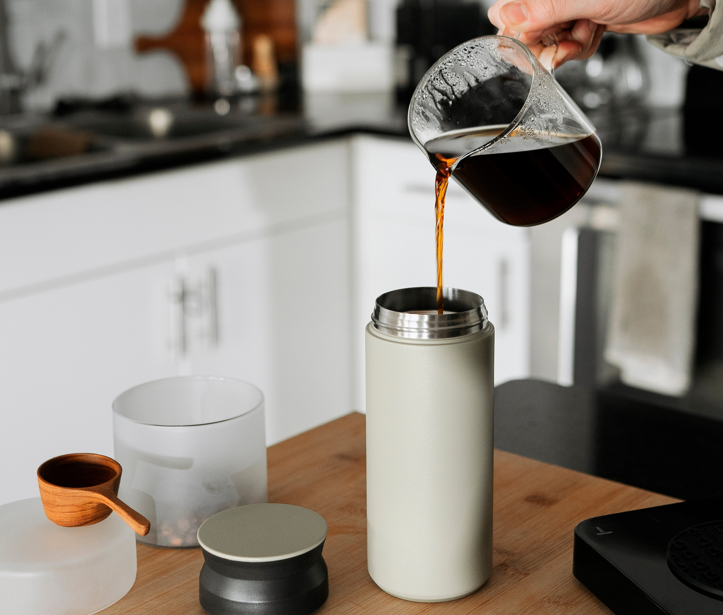 Eine Hand gießt Kaffee aus einem Glasbehälter in einen hellgrünen Thermosbecher.