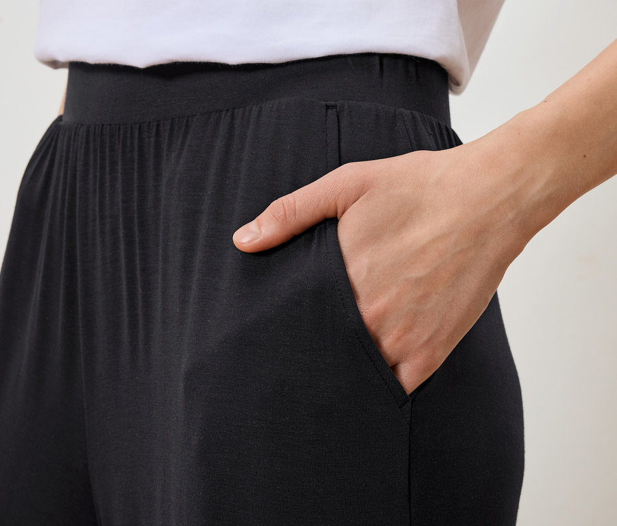 Frau steckt Hand in die Tasche einer schwarzen Hose.