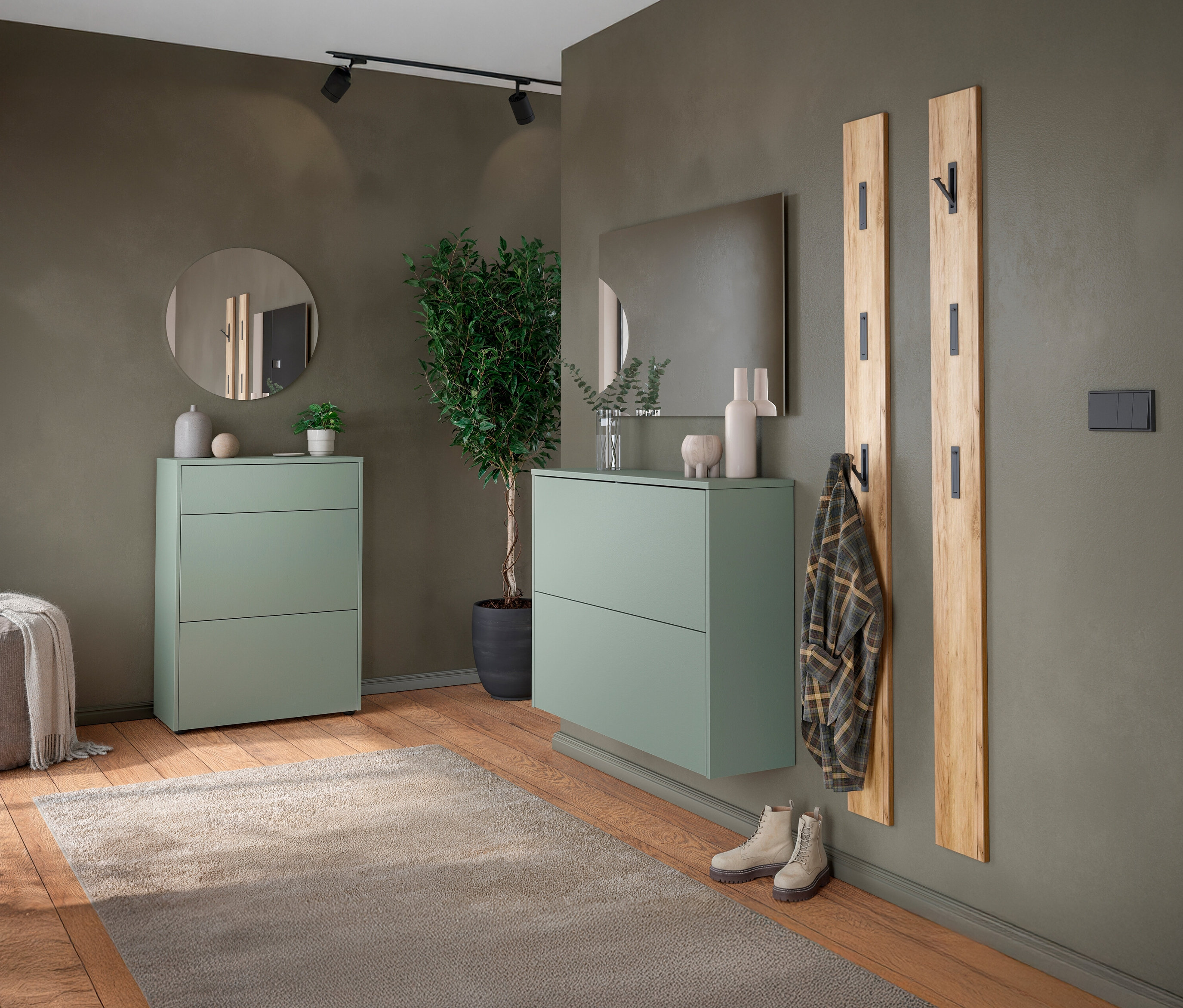 Eingangsbereich mit grünem Schuhschrank, Spiegel und Holzgarderobe an einer olivgrünen Wand.