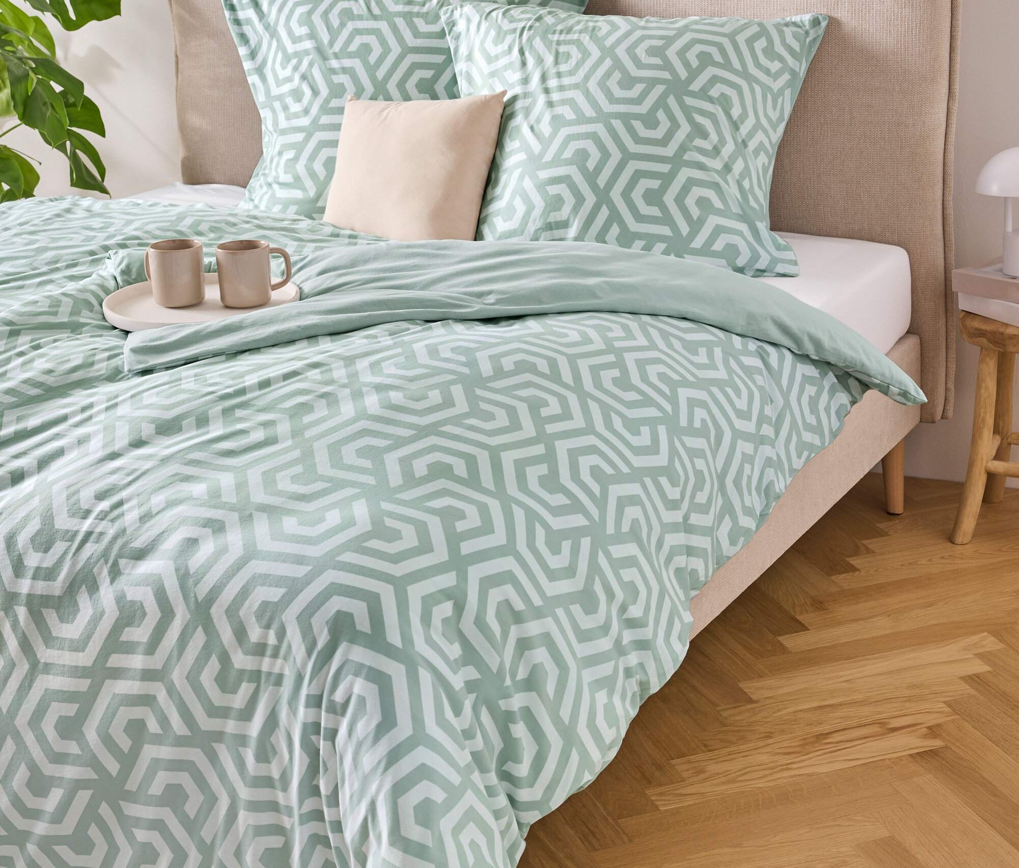 Ein Bett mit hellblau-weiß gestreifter Bettwäsche, zwei Kissen und einer Ablage mit zwei Tassen darauf.