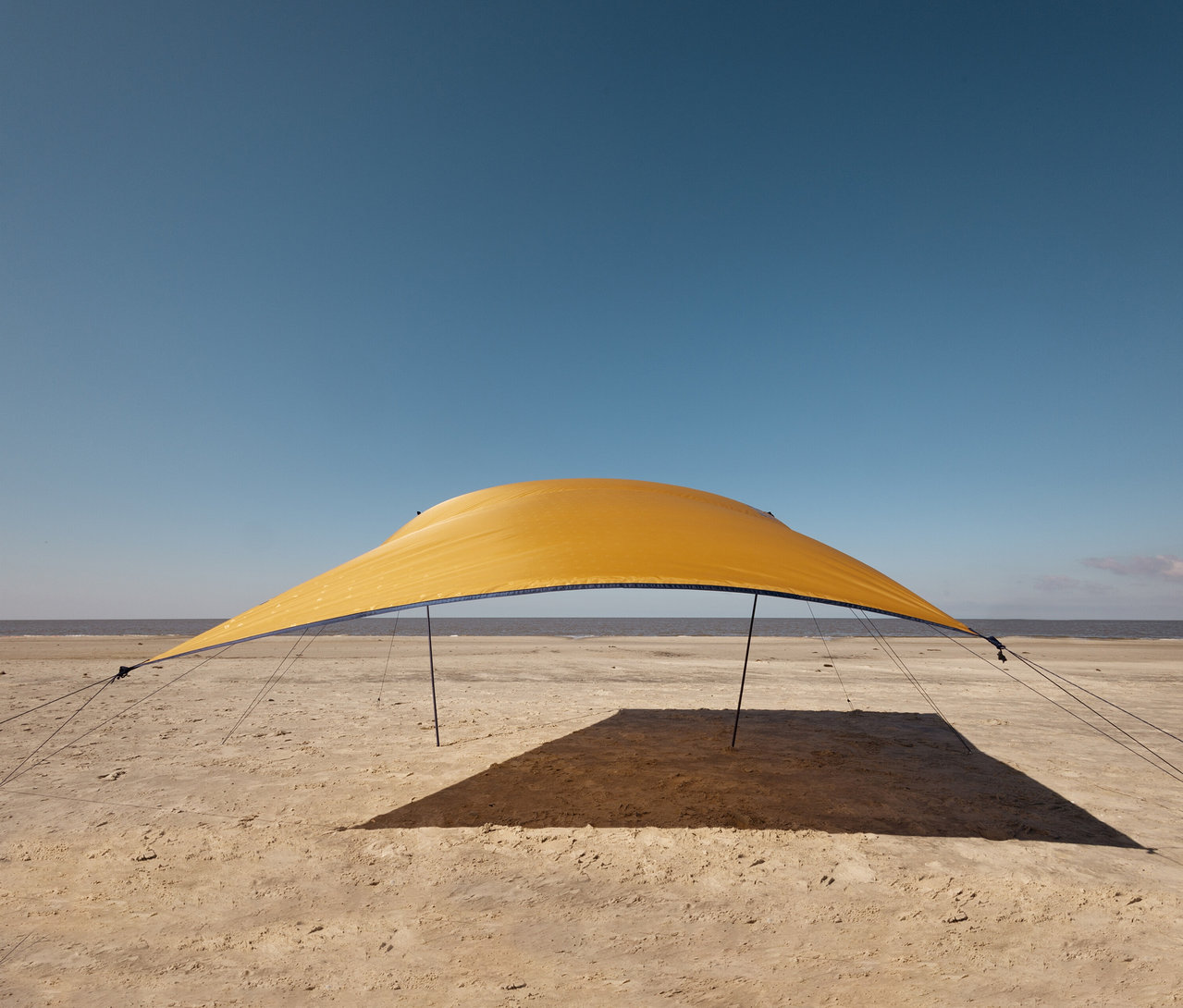 Gelbes Tambu »CHADA« Tarp/Sonnensegel steht am Strand unter blauem Himmel.