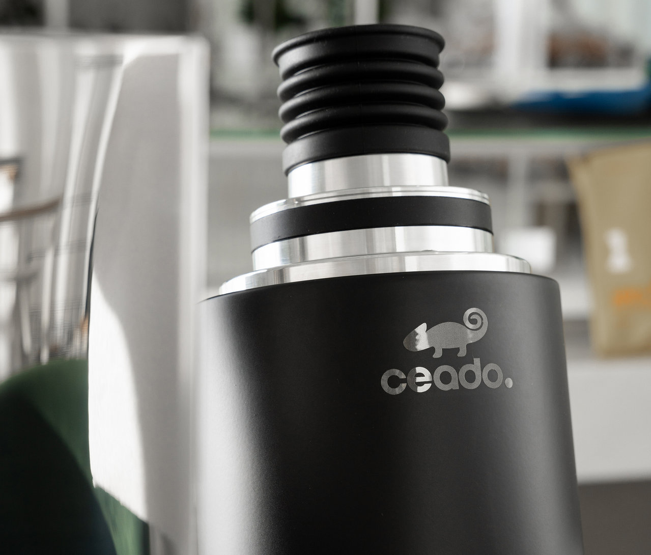 Nahaufnahme einer schwarzen Ceado-Kaffeemühle mit silbernem Logo, daneben ein silberner Behälter.