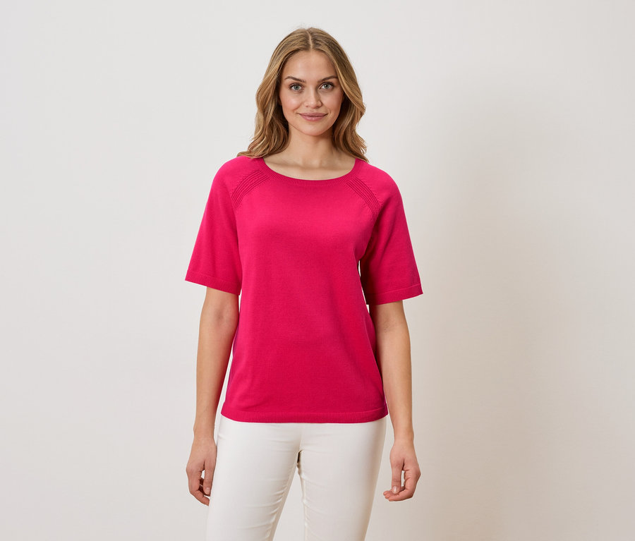 Frau trägt ein pinkes T-Shirt und weiße Hosen.