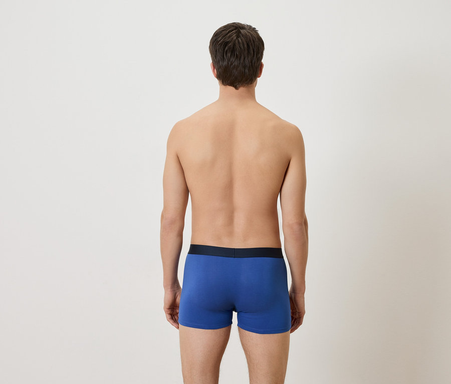 Ein Mann steht mit dem Rücken zur Kamera und trägt blaue Boxershorts.