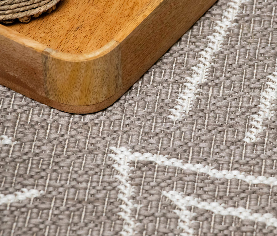 Nahaufnahme einer Ecke eines Holztabletts auf einem grauen Teppich mit weißem Muster.