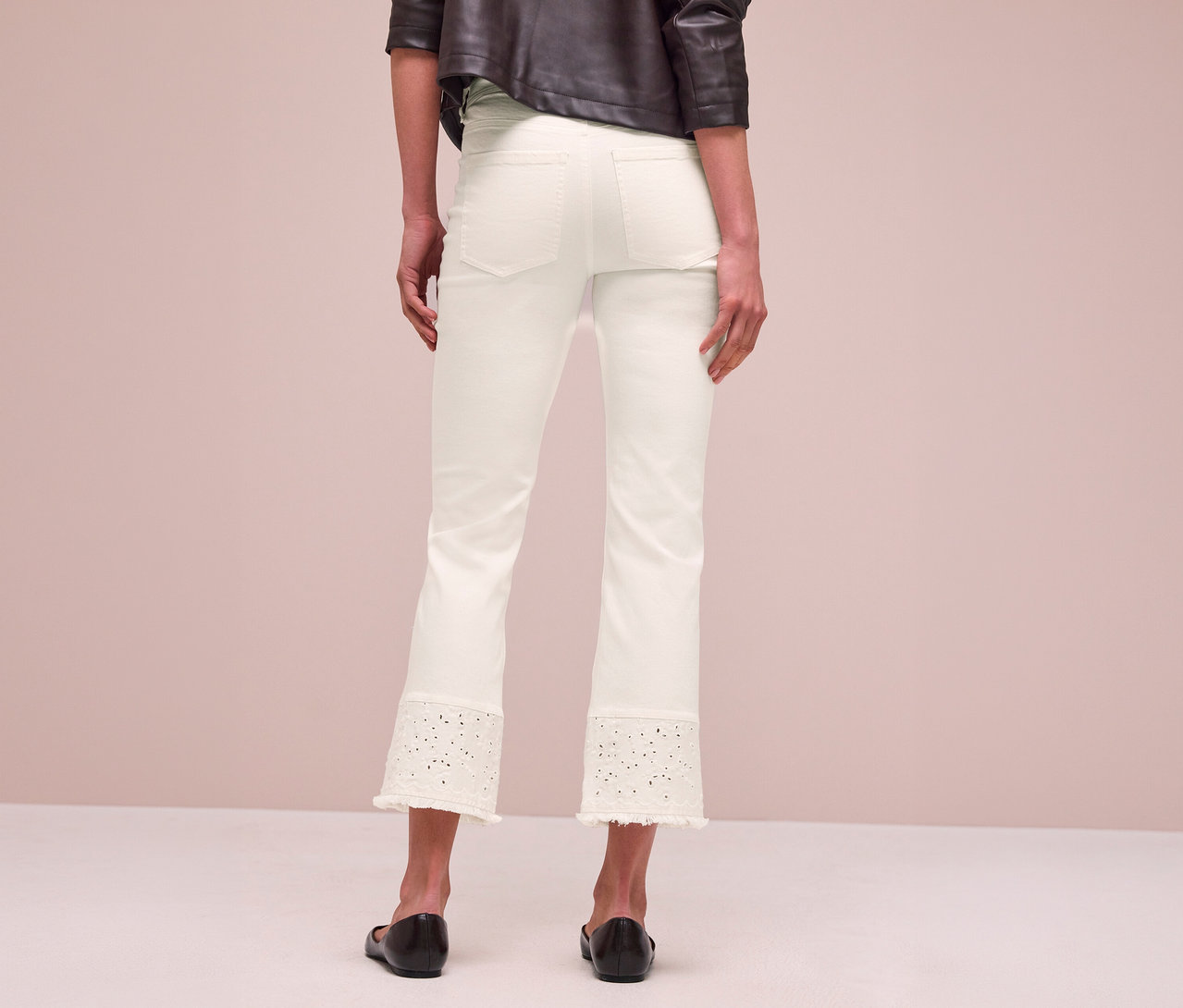 Eine Person von hinten, die weiße Street One Jeans mit bestickten, perforierten Details und ausgefransten Säumen sowie schwarze flache Schuhe trägt.