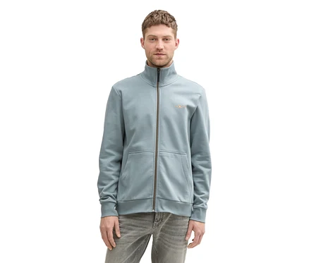Mann trägt eine mintgraue Tom Tailor Sweatjacke mit Stehkragen und graue Jeans.
