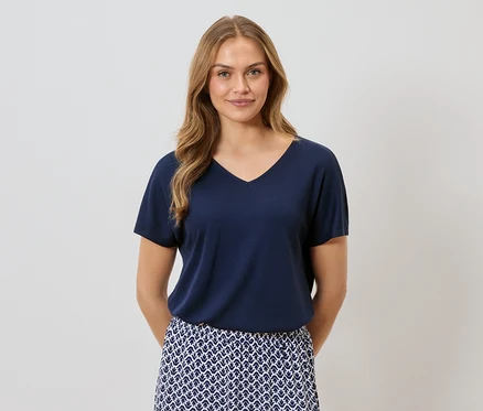 Frau mit blonden Haaren, die ein marineblaues T-Shirt und einen blau-weiß gemusterten Rock trägt.