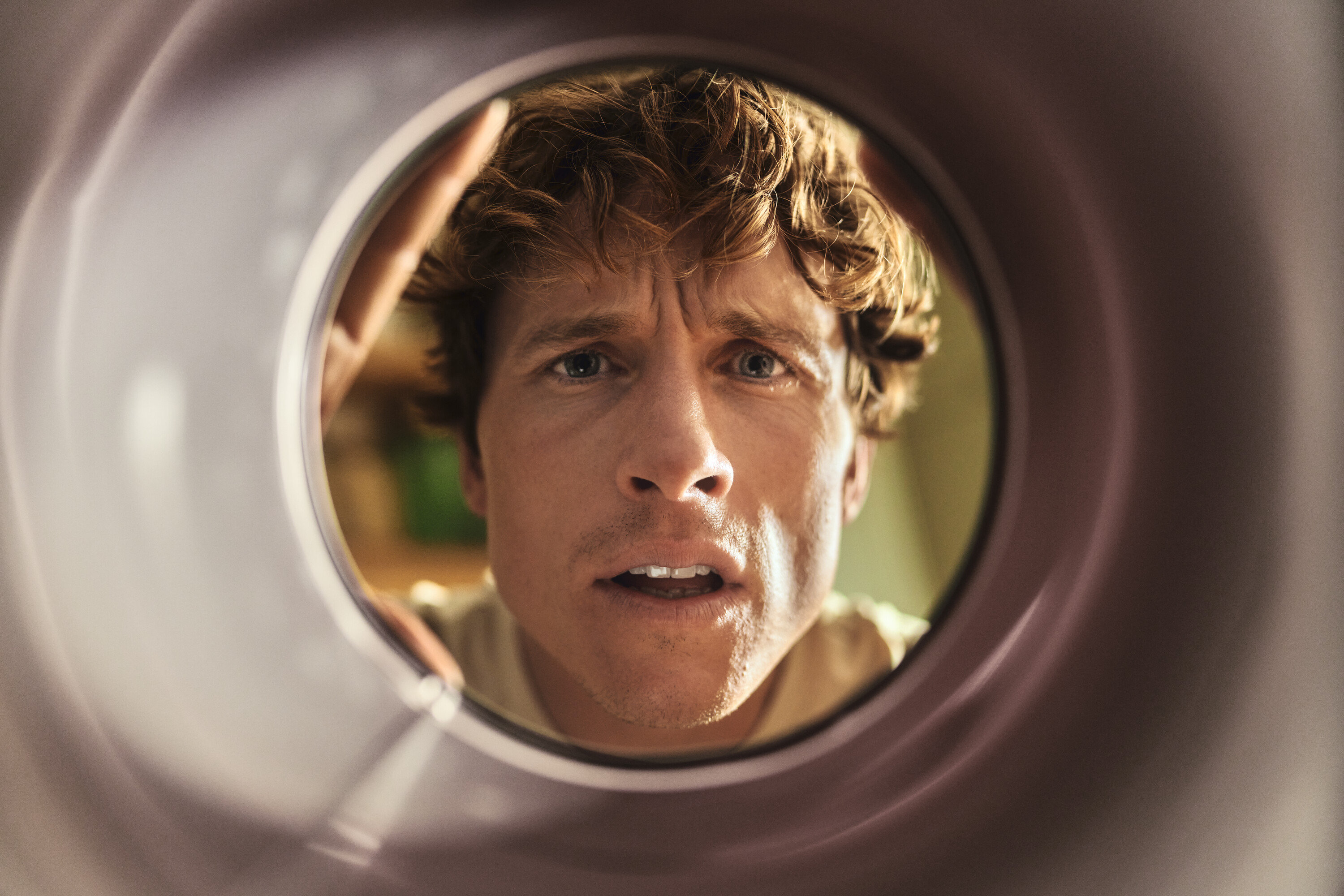 Ein Mann mit lockigem Haar blickt besorgt in eine runde Öffnung.