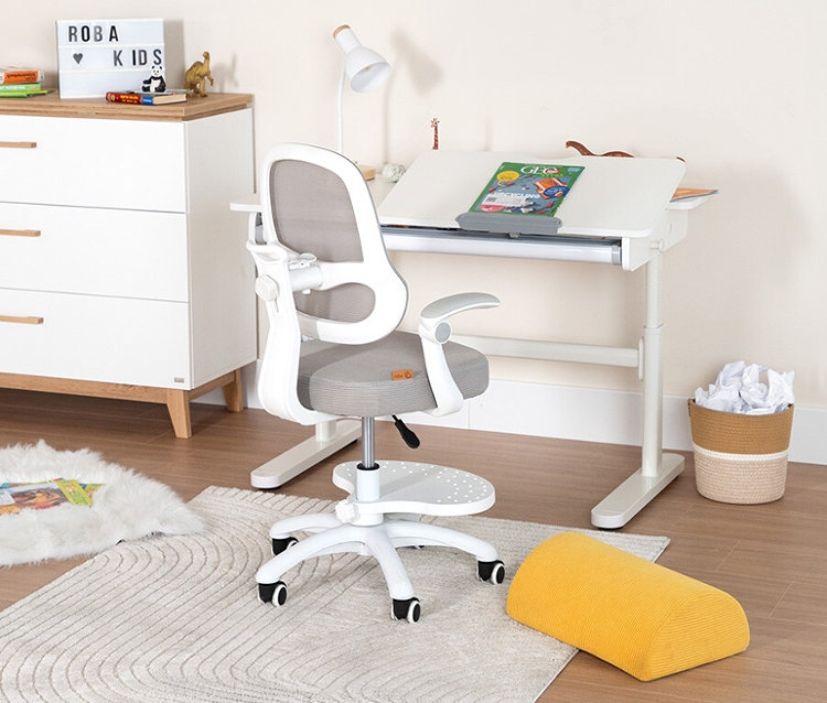 Ein Kinderzimmer zeigt einen Schreibtisch mit Stuhl, Lampe und Deko. Neben dem Schreibtisch steht eine Kommode und ein Papierkorb.