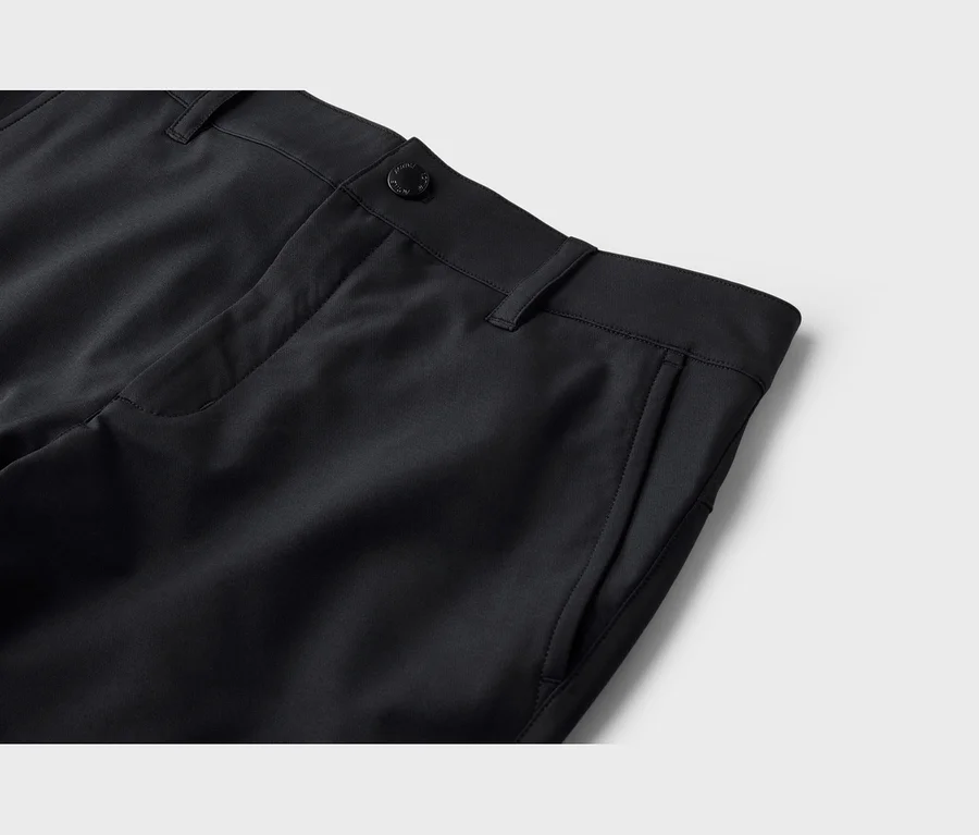 Nahaufnahme der oberen rechten Seite einer schwarzen Hose, die den Bund, einen schwarzen Knopf, Gürtelschlaufen und eine Seitentasche zeigt. Der Stoff ist glatt.
