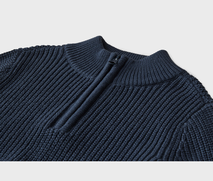Nahaufnahme eines marineblauen Strickpullovers mit Rippenstruktur und Stehkragen, der einen dunklen Viertelreißverschluss hat.