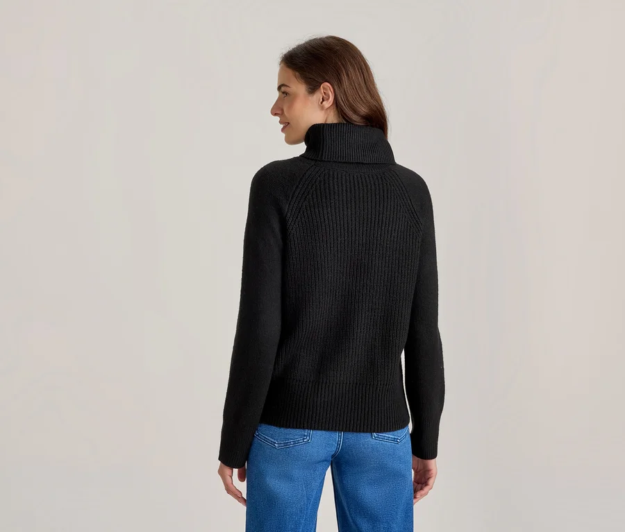 Frau von hinten, leicht zur Seite gedreht, trägt einen schwarzen Rollkragenpullover und blaue Jeans.