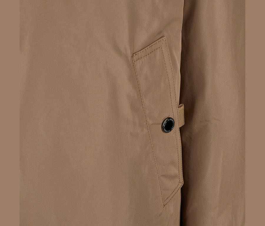 Nahaufnahme einer beigen Barbara Lebek Kurzjacke, die eine Taschenklappe mit schwarzem Knopf und kleiner Stoffschlaufe zeigt.
