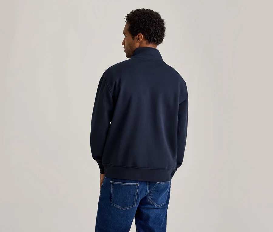 Mann von hinten gesehen, trägt ein marineblaues Quarter-Zip-Sweatshirt und blaue Jeans. Er hat lockiges dunkles Haar und blickt nach rechts.