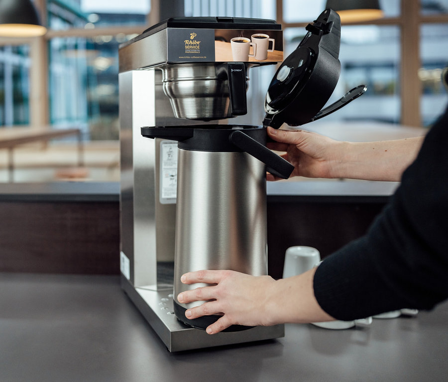 Person bedient Profi-Filterkaffeemaschine »Tchibo Businessline« ohne Kanne mit »Crem Thermo Tchibo Businessline« Spar-Set.
