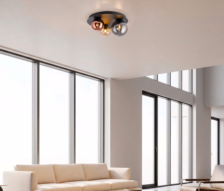 Eine moderne Deckenleuchte mit schwarzer Basis und drei kugelförmigen Glasschirmen in Roségold, Bernstein und Rauchgrau, installiert in einem hellen Wohnzimmer mit großen Fenstern.