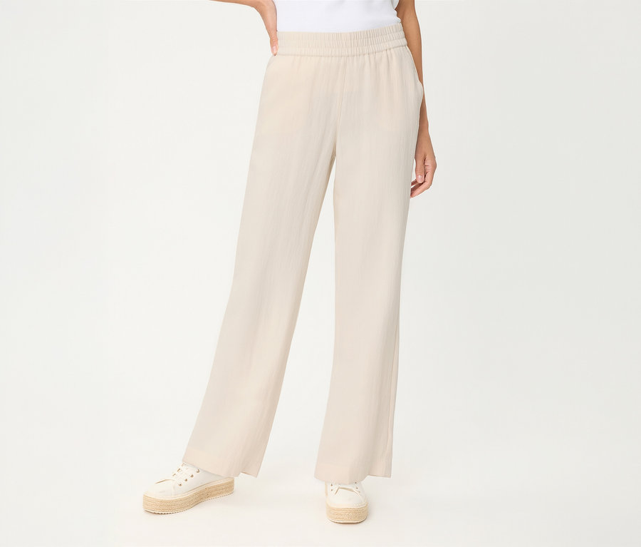 Person trägt hellbeige Olsen Leinenhose mit weitem Bein und Gummibund, dazu weiße Espadrille-Sneaker.