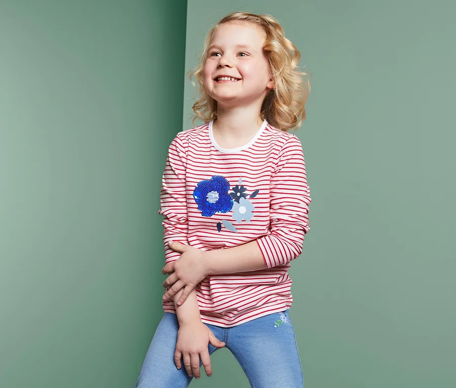 Lächelndes Mädchen trägt ein Langarmshirt mit Wendepailletten.