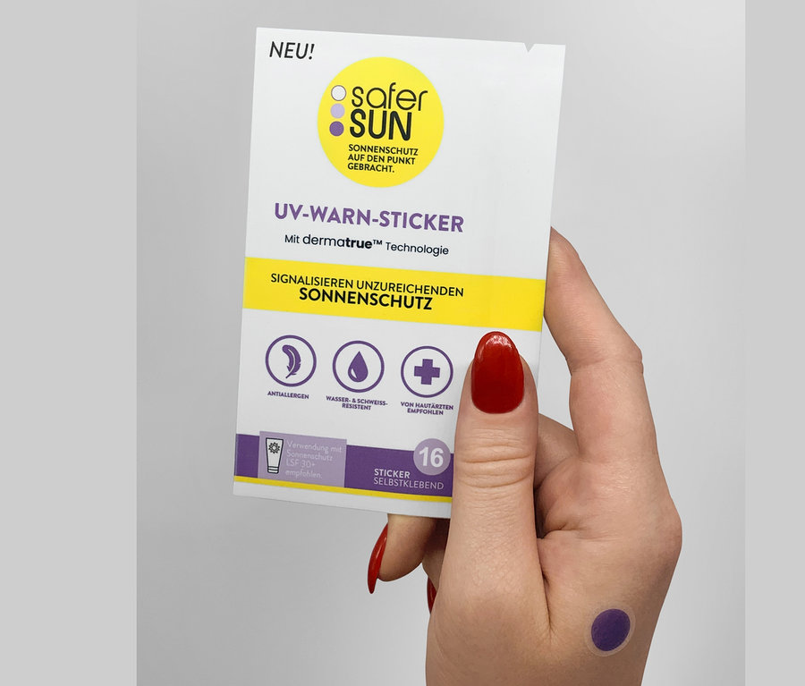 Frau hält eine Packung mit 16 UV-Warnstickern von Safer Sun. Auf ihrem Handrücken klebt ein violetter Sticker.