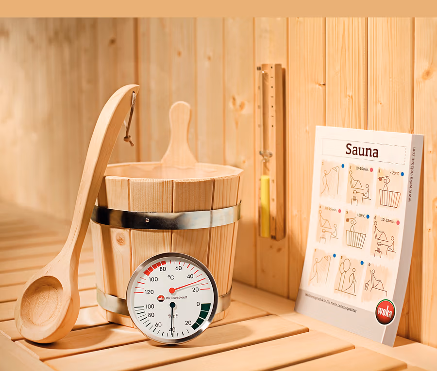 Innenraum einer Sauna mit Holzeimer, Schöpfkelle, Thermometer und WEKA-Infobroschüre.